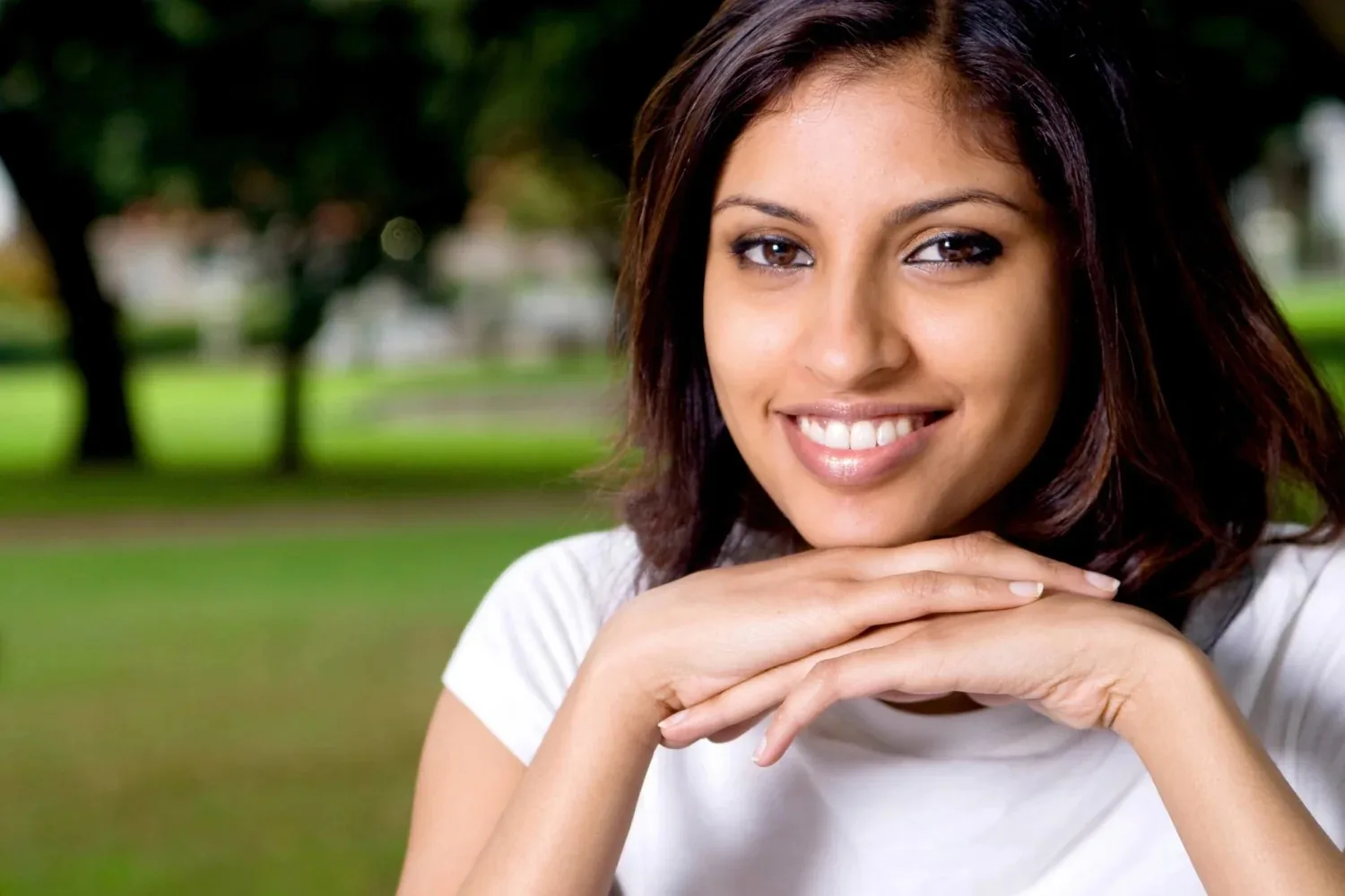 A smiling adult resting their chin on their hands in a park.